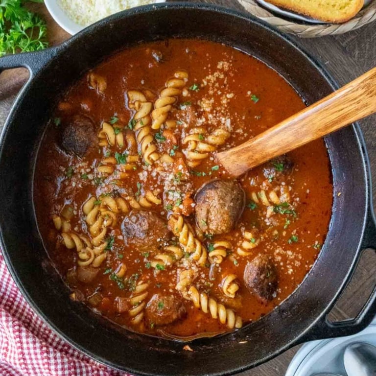 Italian meatball soup with a wooden spoon in a pot.
