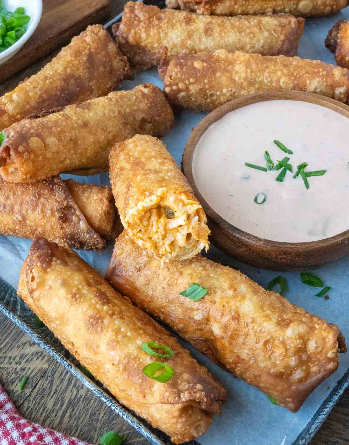 A serving dish with buffalo chicken egg rolls and dipping sauce.
