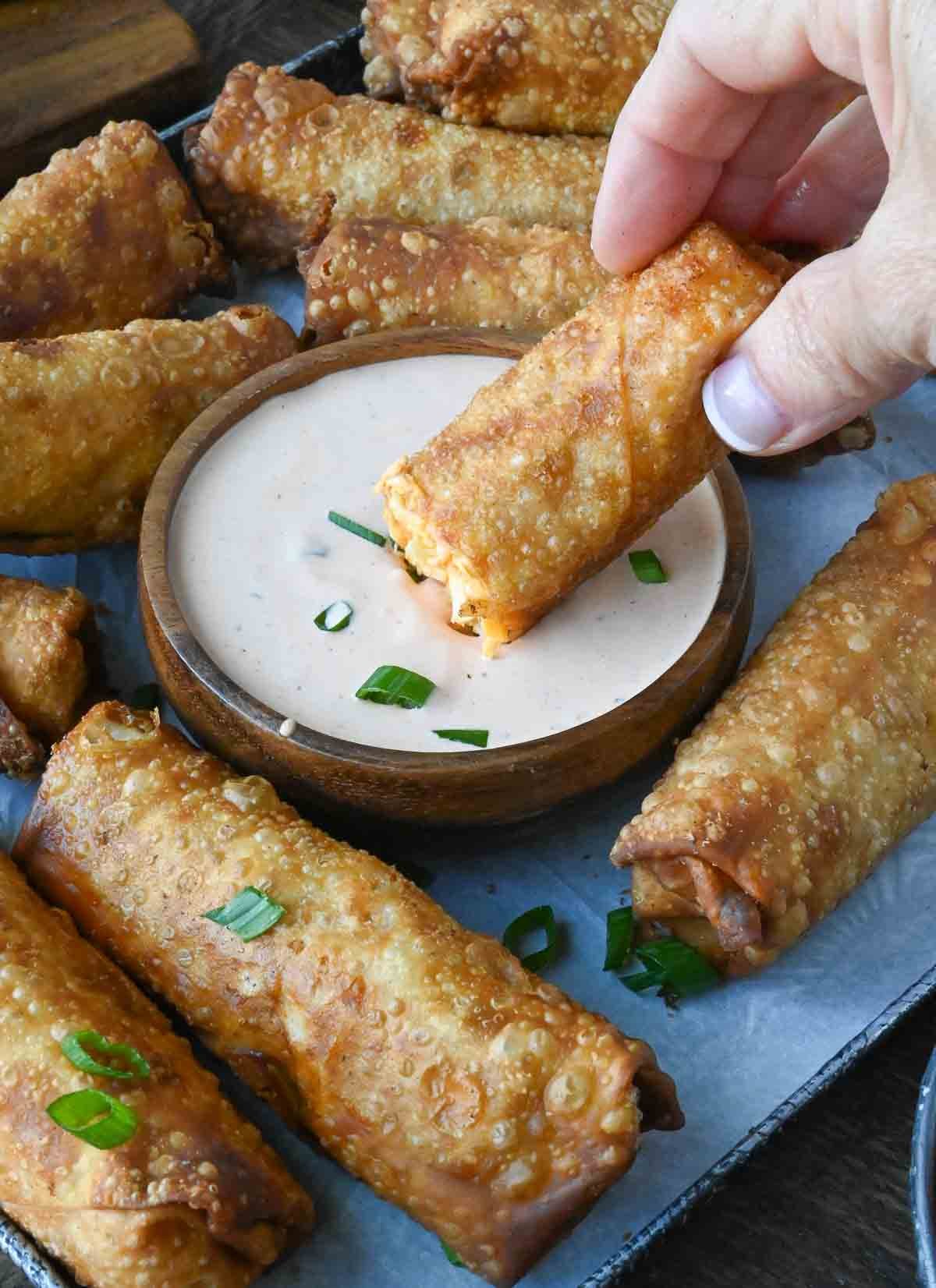 A plate of egg rolls with a hand dipping one into a dish of sauce.