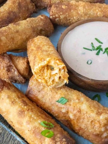 Close up of a serving tray of buffalo chicken eggrolls with dipping sauce on the side.