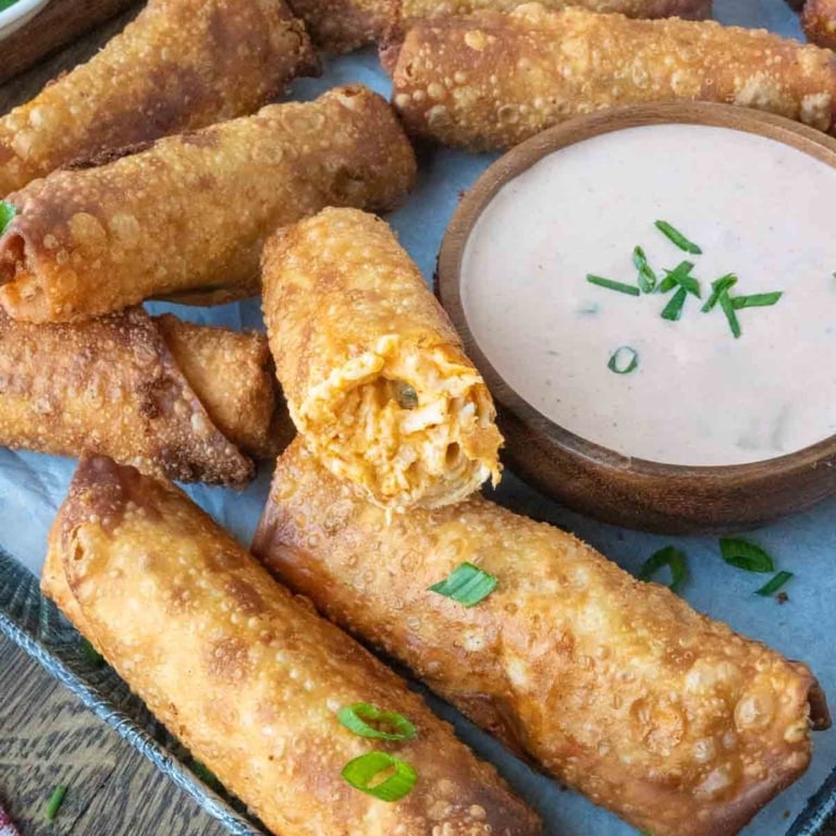 Close up of a serving tray of buffalo chicken eggrolls with dipping sauce on the side.
