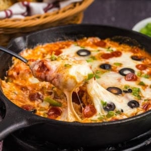 Pizza dip in a skillet with a spoon scooping some out