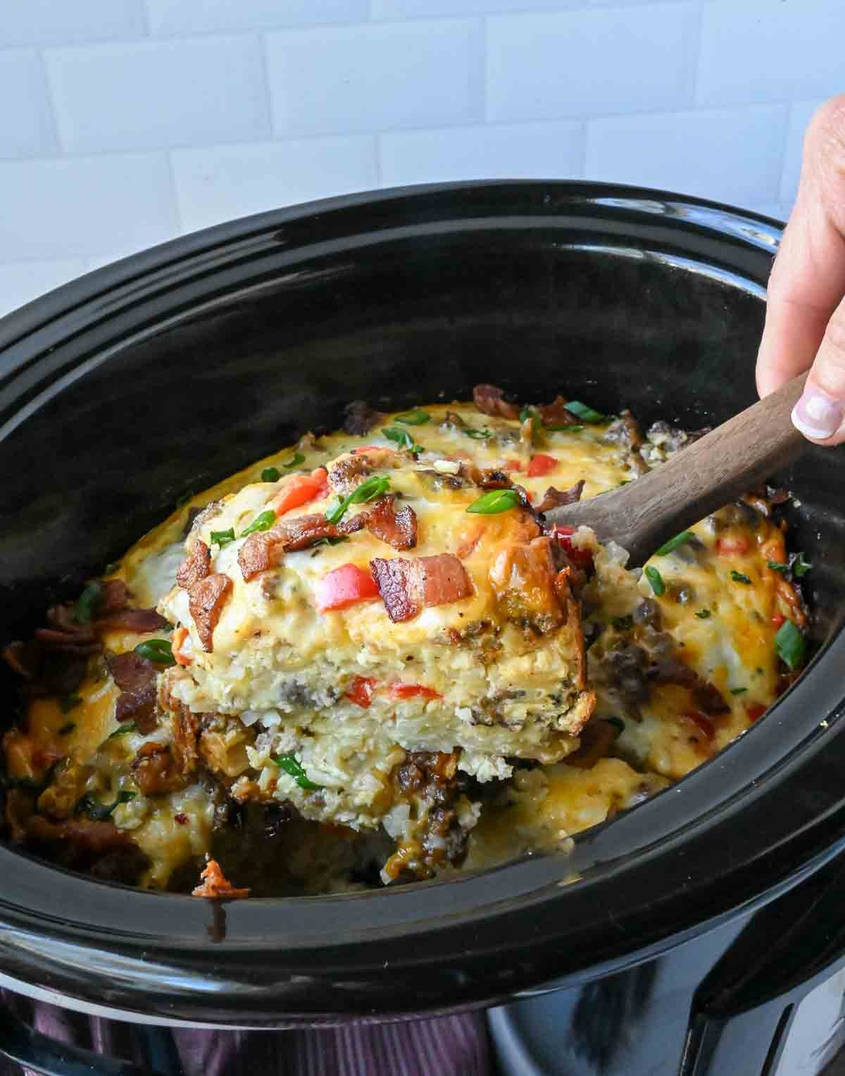 Taking a scoop of crock pot breakfast casserole from a slow cooker.