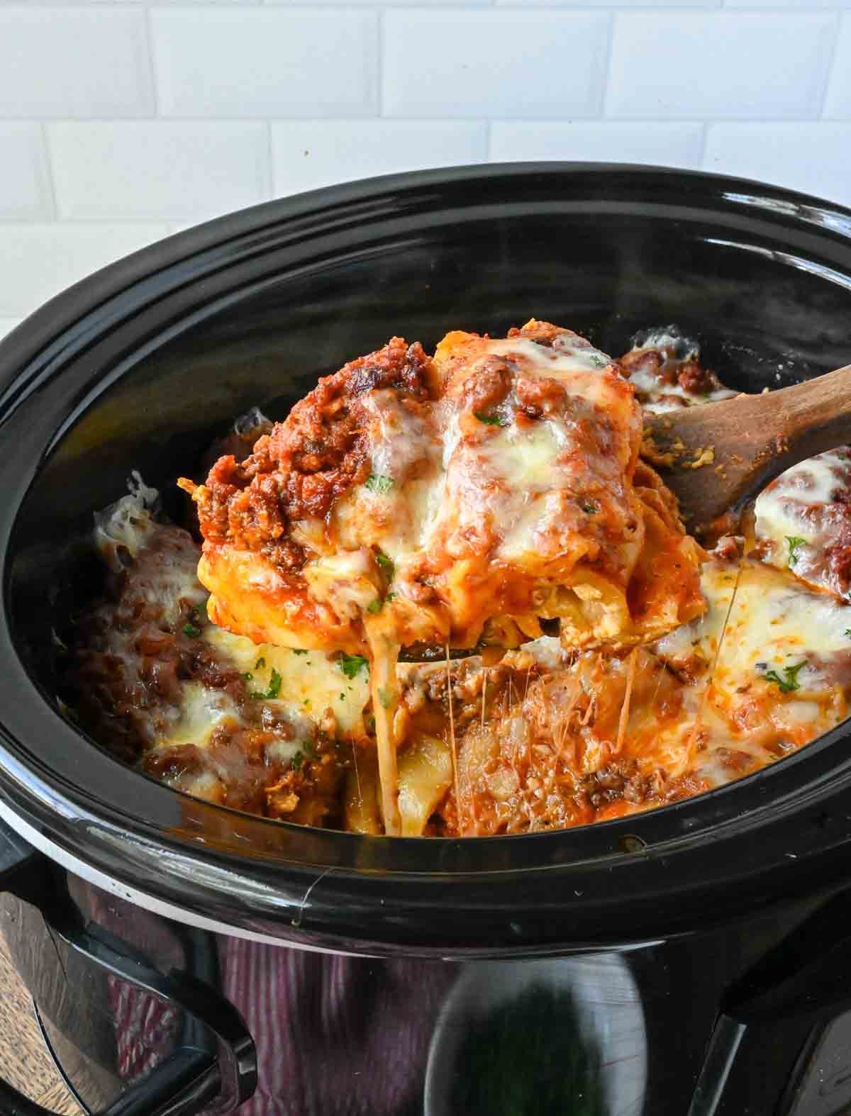 Taking a scoop of crockpot lasagna with a wooden spoon.