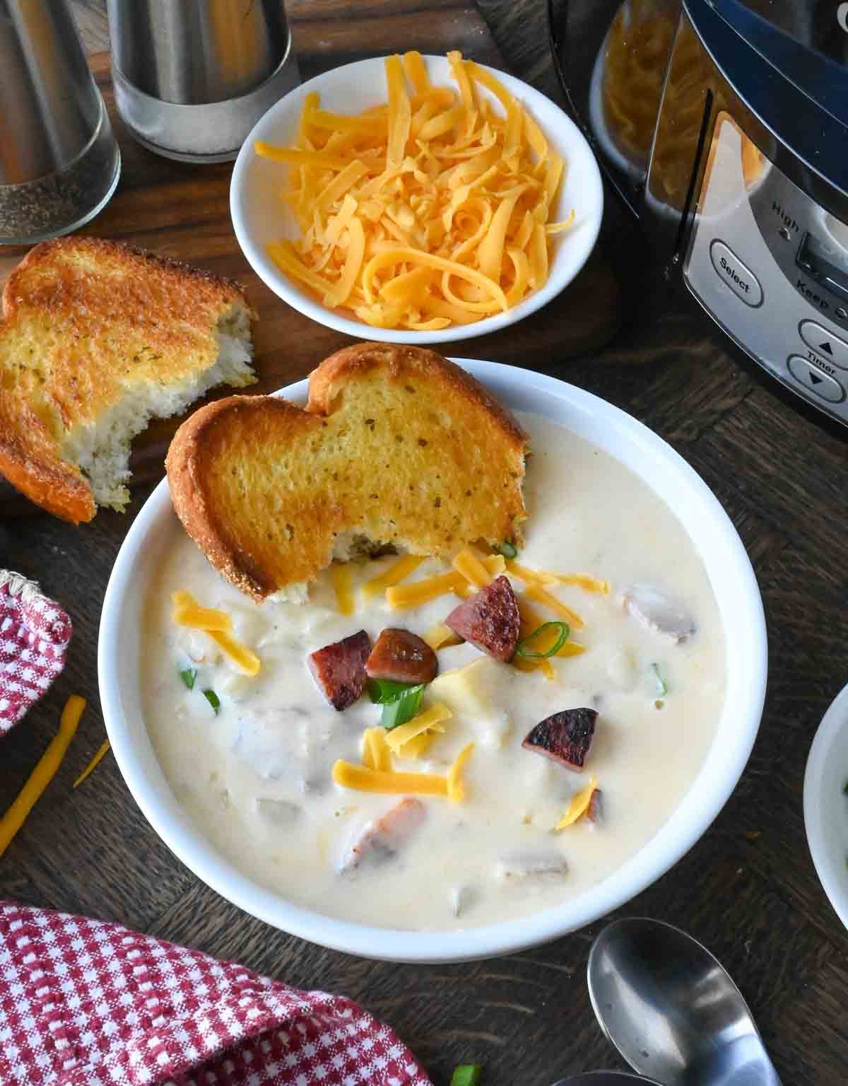 A bowl of kielbasa potato soup with texas toast and shredded cheese.