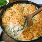 Taking a scoop of chicken and biscuit casserole from a cast iron skillet.