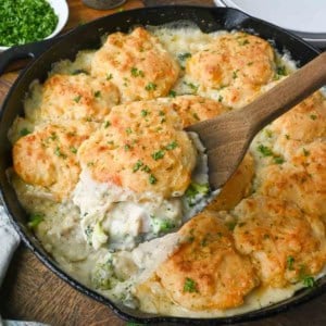 Taking a scoop of chicken and biscuit casserole from a cast iron skillet.