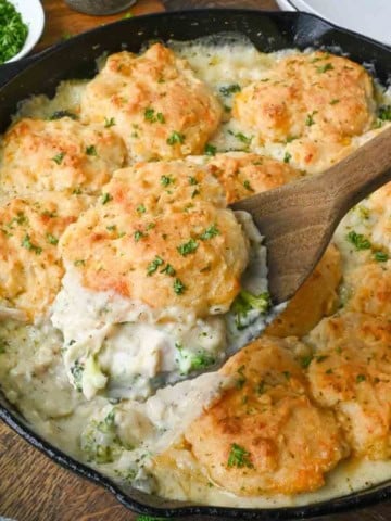 Taking a scoop of chicken and biscuit casserole from a cast iron skillet.