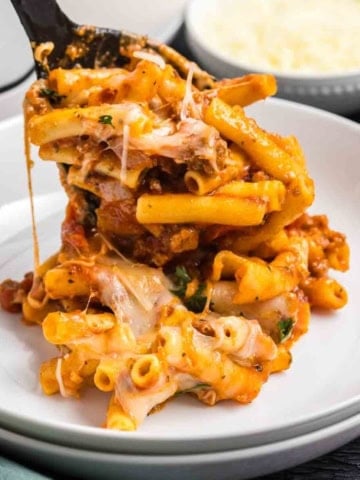 Spooning slow cooker baked ziti onto a white plate.