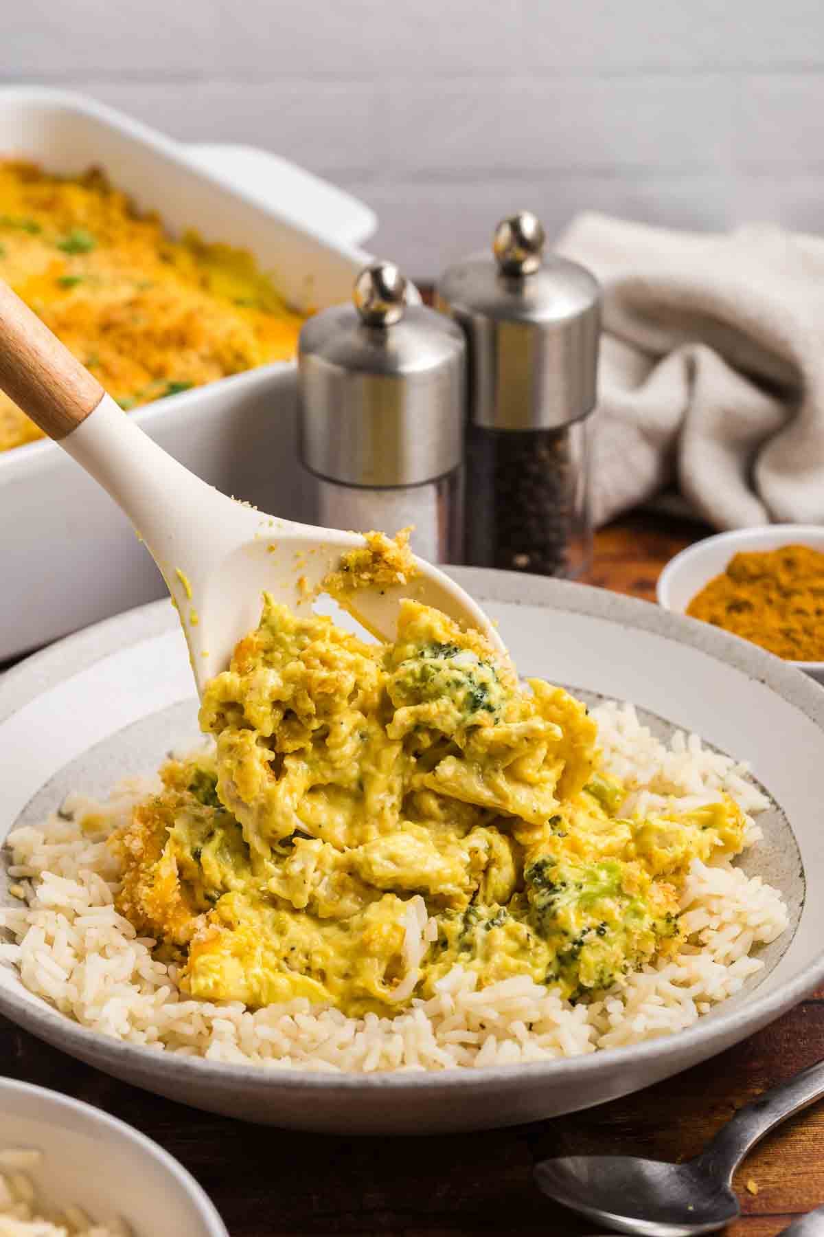 Spooning chicken divan casserole onto a plate of rice.