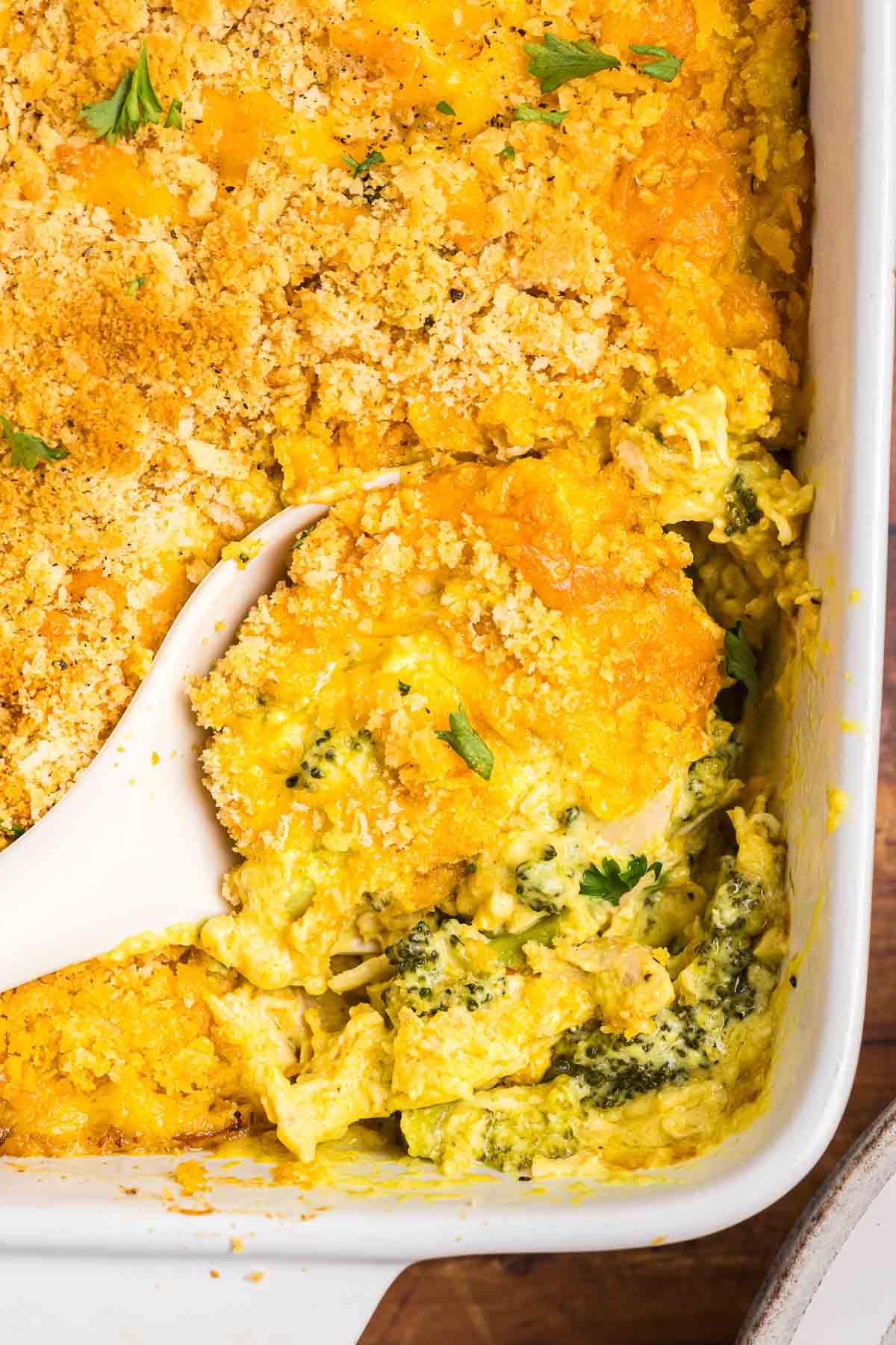Taking a scoop of broccoli chicken divan casserole with a wooden spoon.