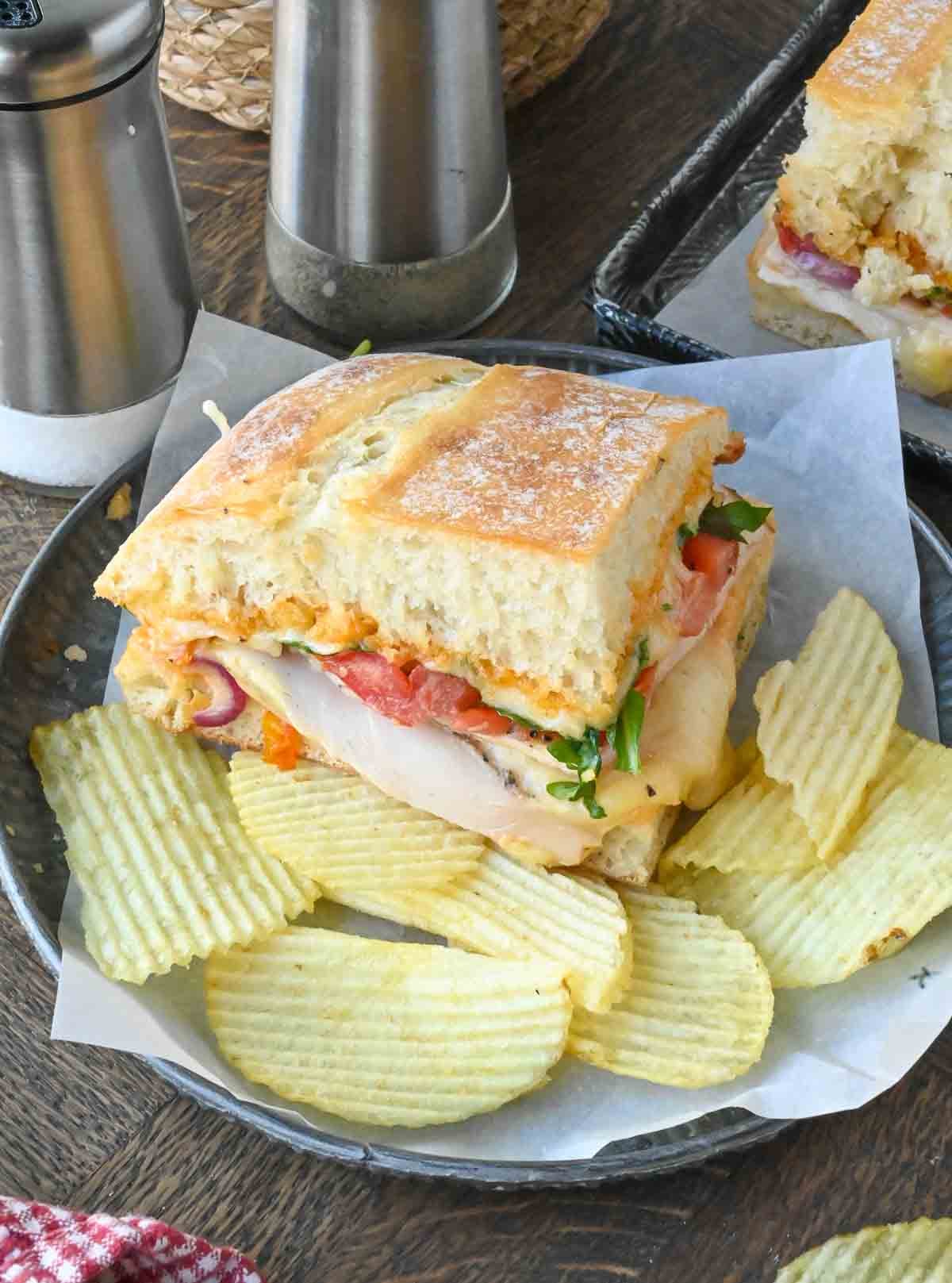 A plate with a ciabatta chicken sandwich and potato chips.