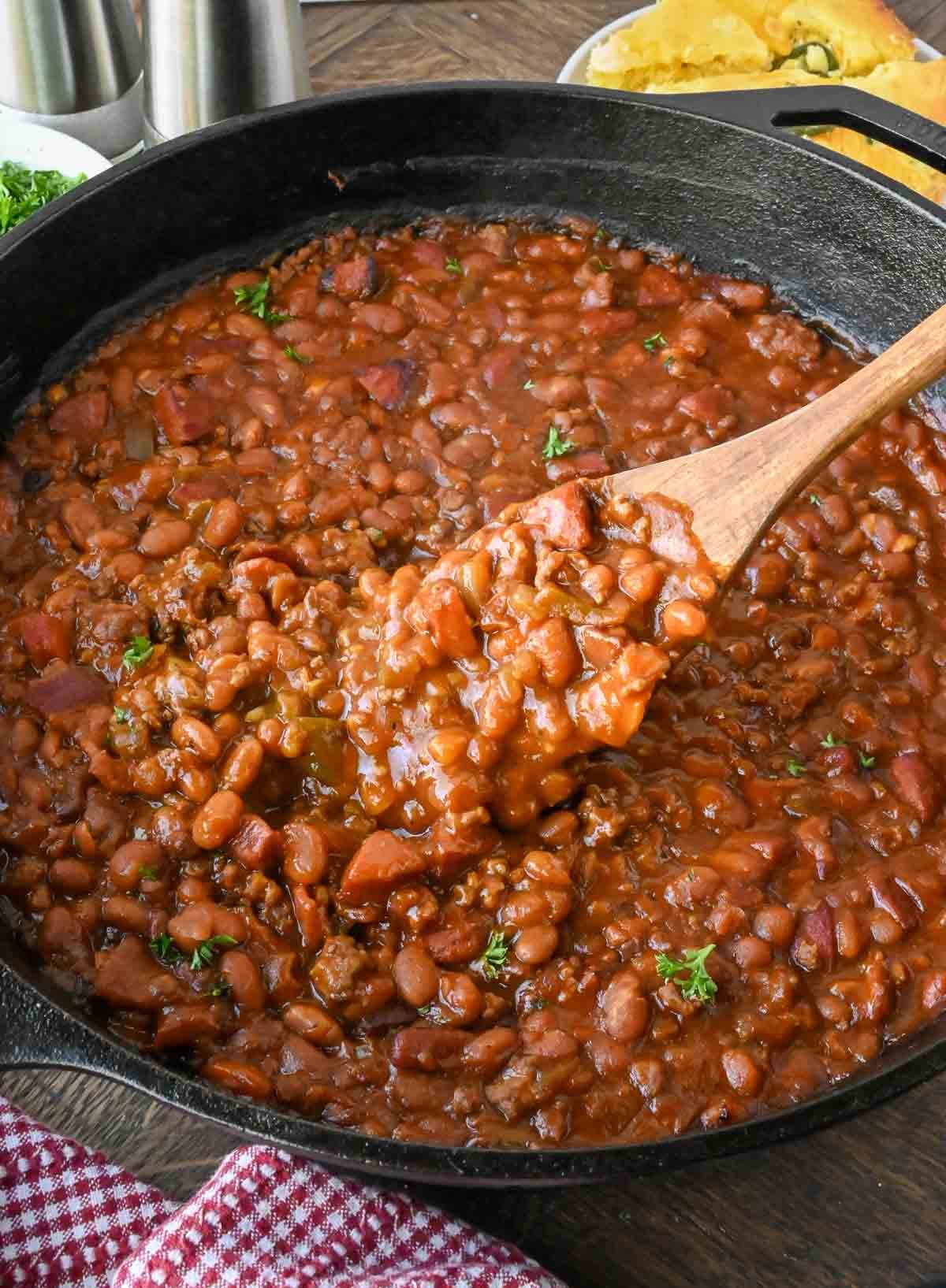 Taking a scoop of cowboy baked beans from a cast iron skillet.