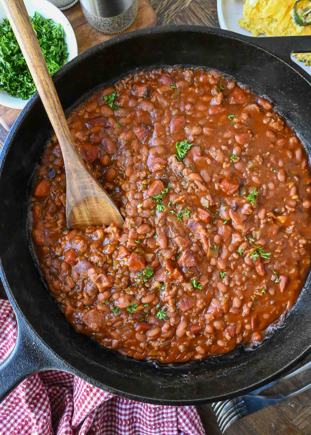 Stirring cowboy baked beans in a skillet with a wooden spoon.