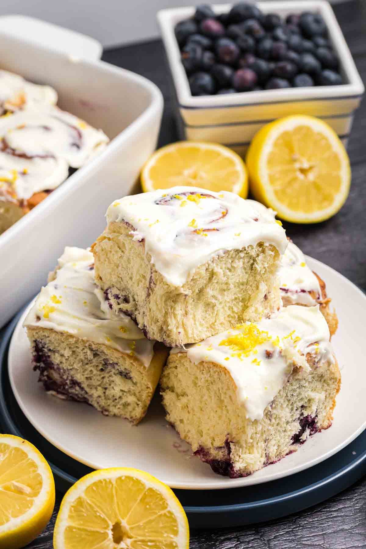 A plate of lemon blueberry rolls with cream cheese frosting and lemon zest garnish.