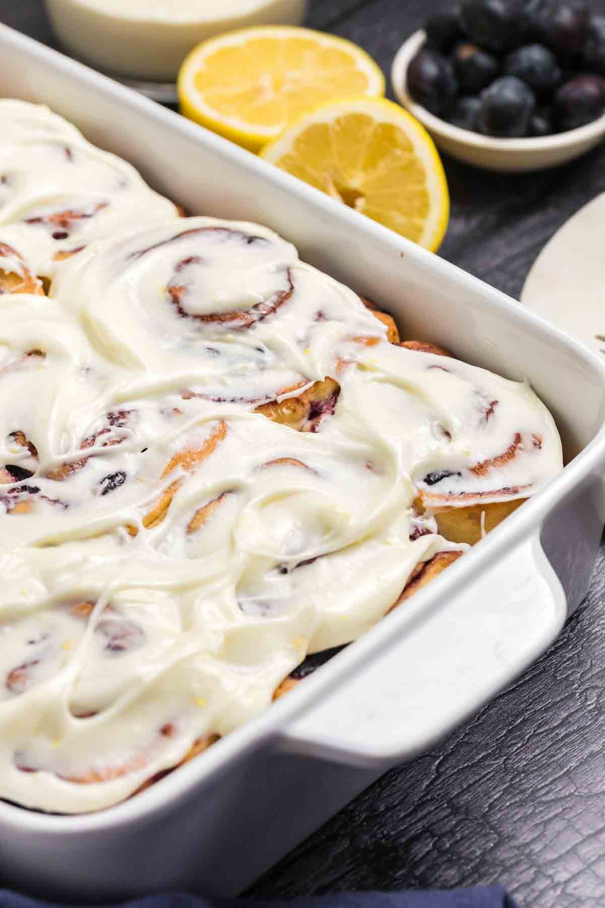 A baking pan filled with lemon blueberry rolls with cream cheese frosting.