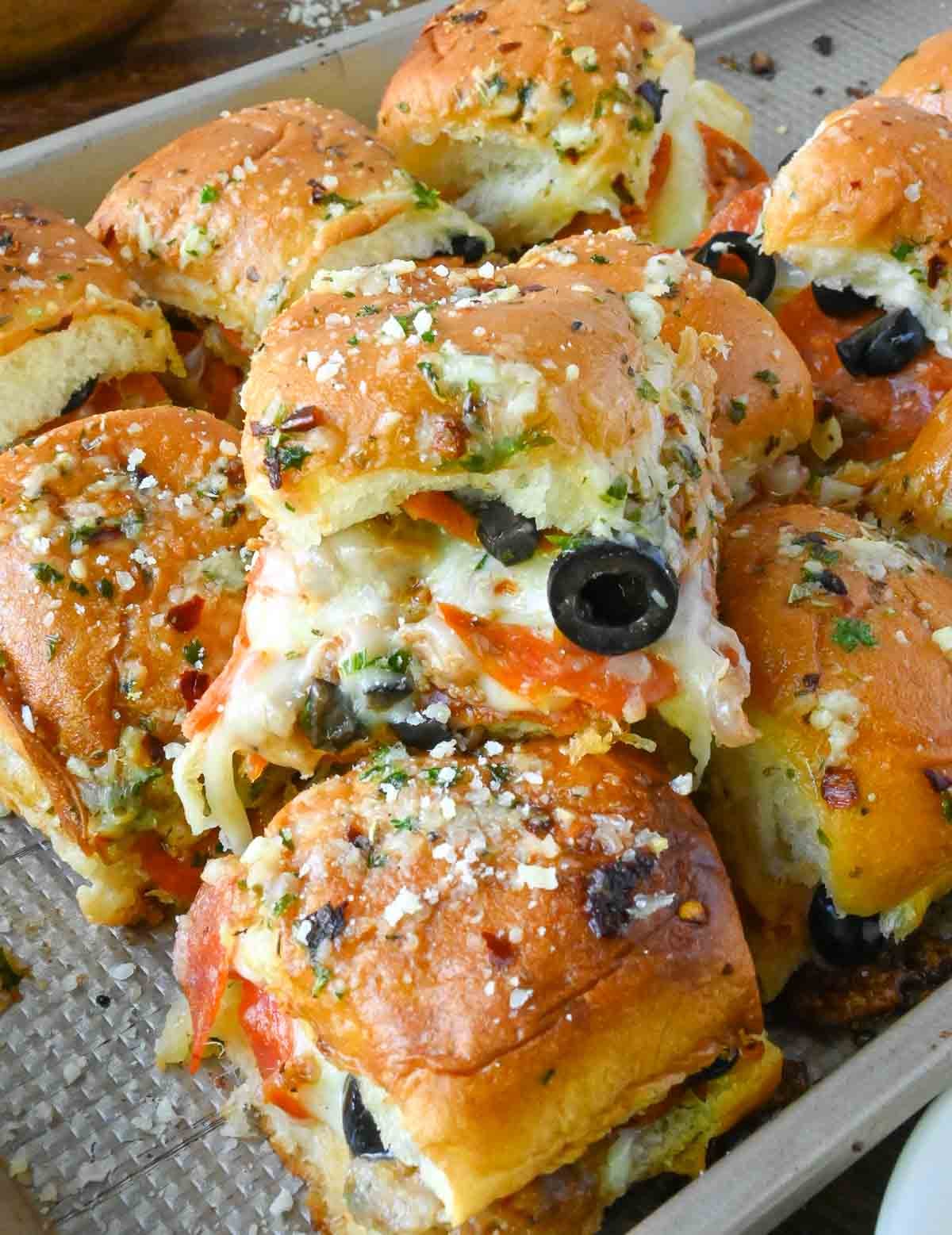 A baking tray stacked with pizza sliders on hawaiian rolls.