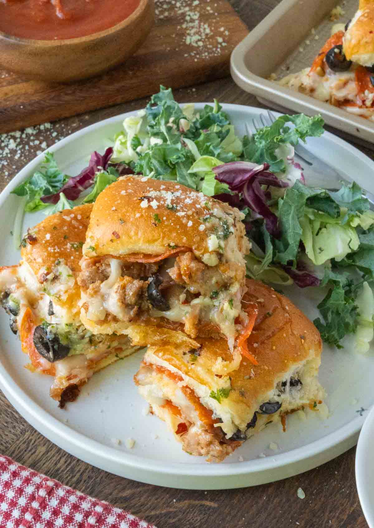 A plate with 3 pizza sliders on hawaiian rolls served with side salad.