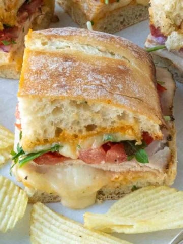 Close up of a half of a chicken ciabatta sandwich with a side of potato chips.