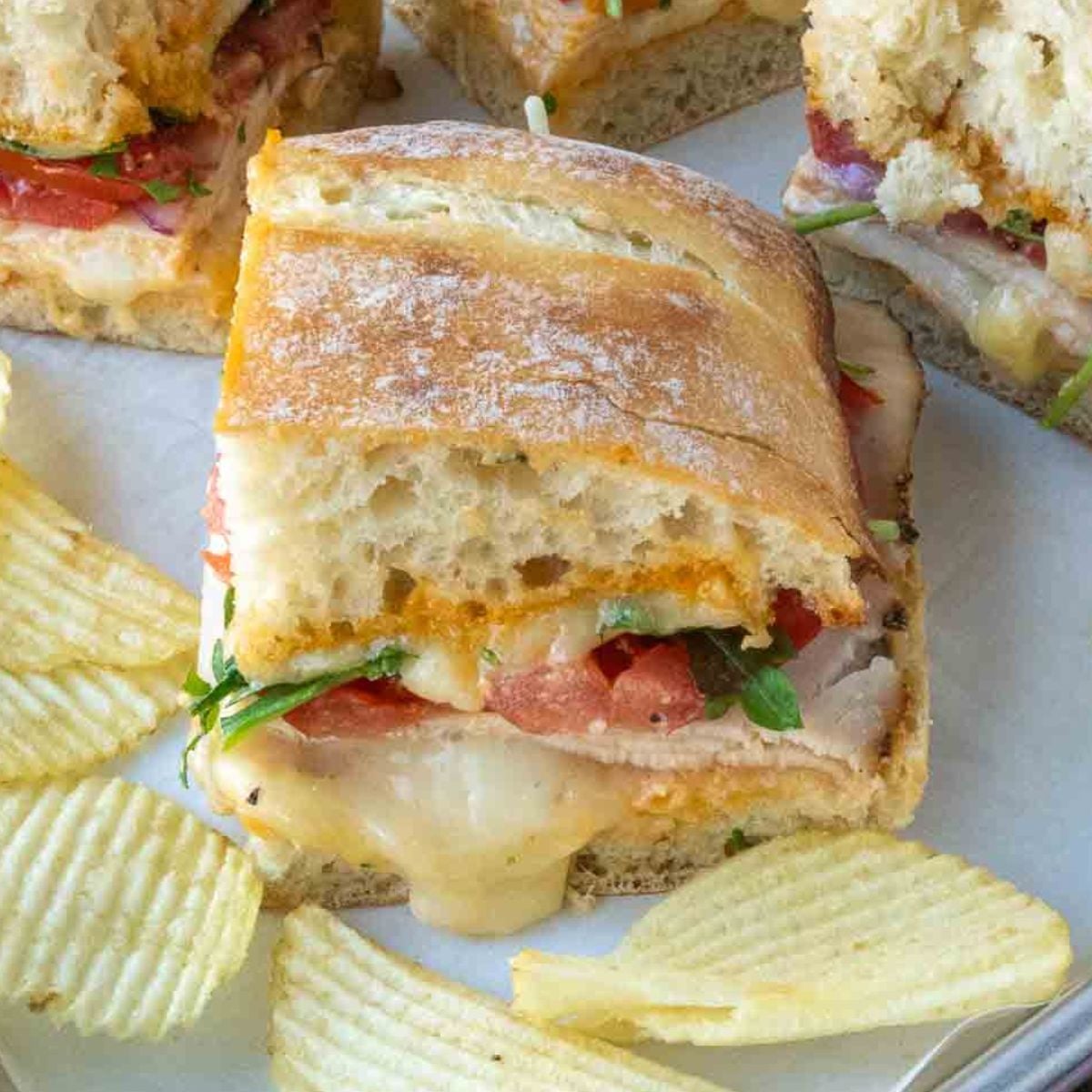 Close up of a half of a chicken ciabatta sandwich with a side of potato chips.