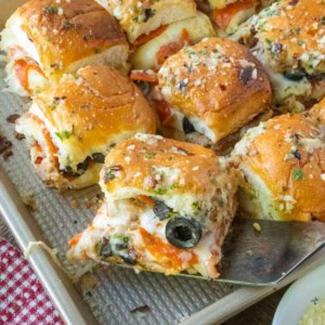 Using a spatula to lift a pizza slider from a tray of sliders.