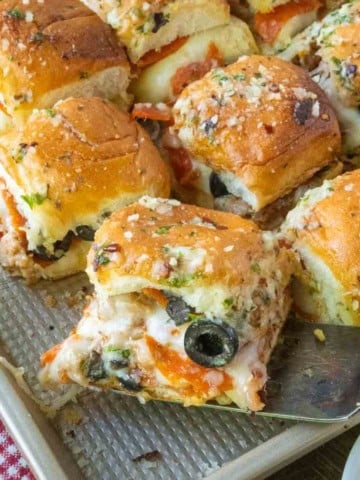 Using a spatula to lift a pizza slider from a tray of sliders.