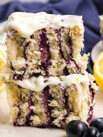 A stack of two lemon blueberry rolls with cream cheese frosting.