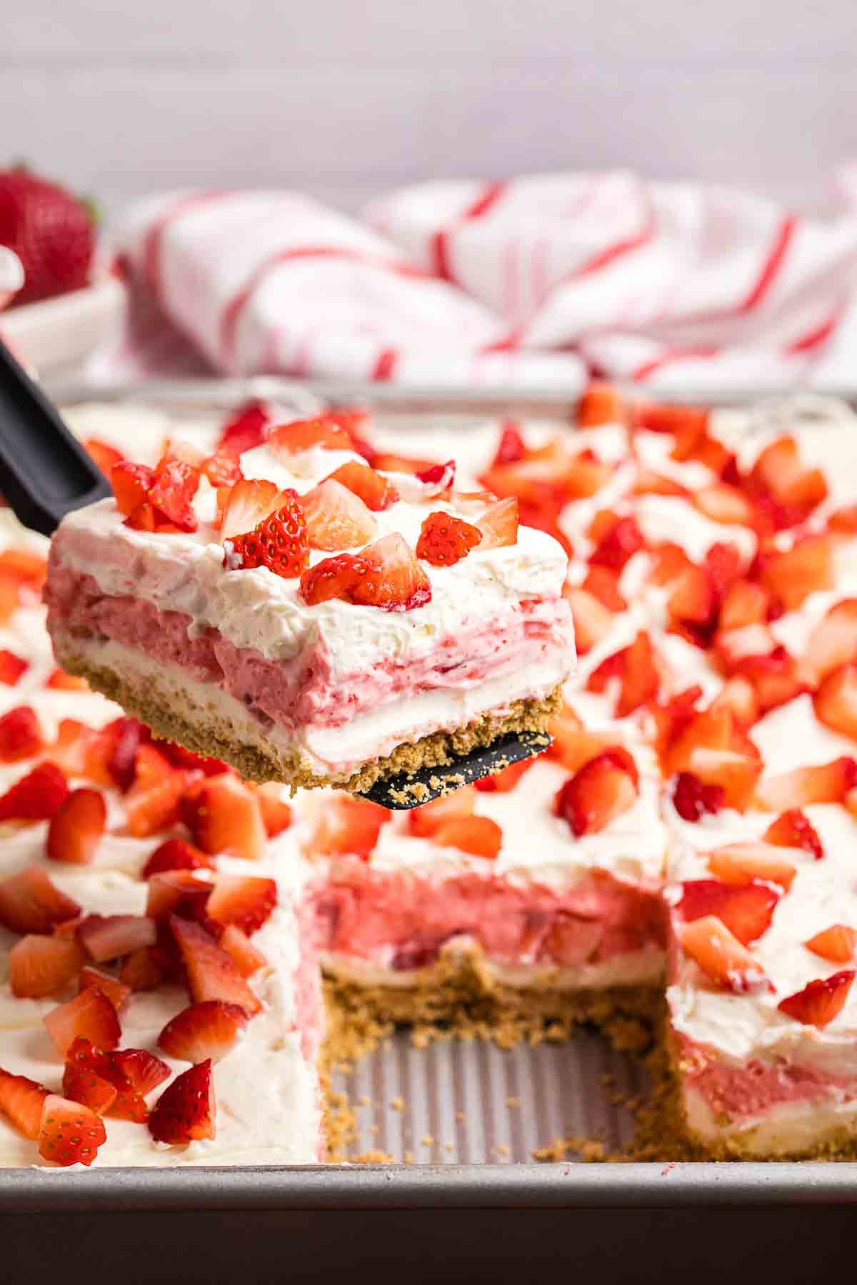 Using a spatula to lift a slice of strawberry delight from a baking pan.