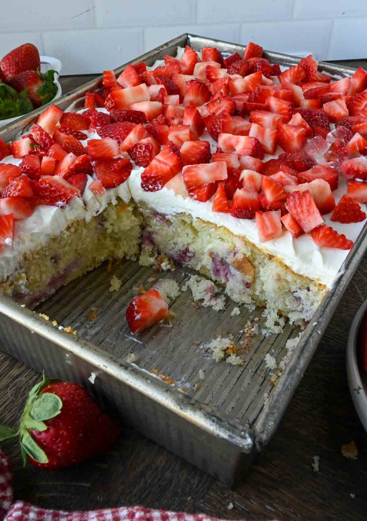 A strawberry whipped cream cake in a baking pan with a few slices missing.