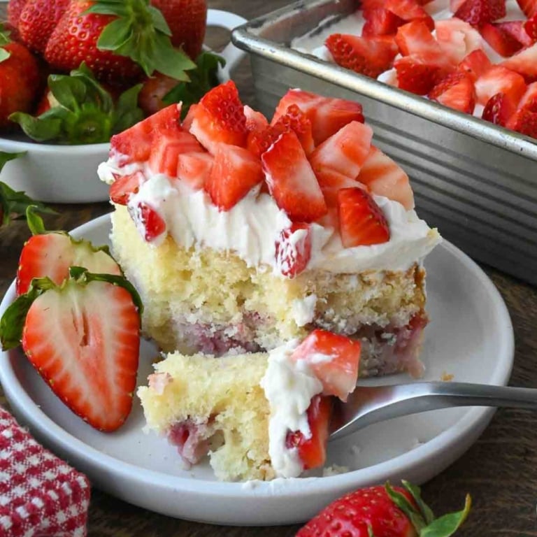 A plate of strawberry whipped cream cake with fresh strawberries.