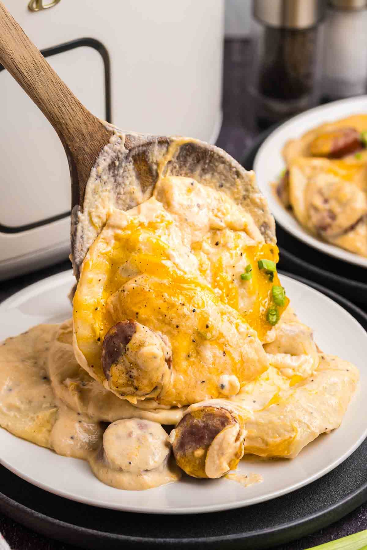 Spooning crockpot pierogi casserole onto a plate.