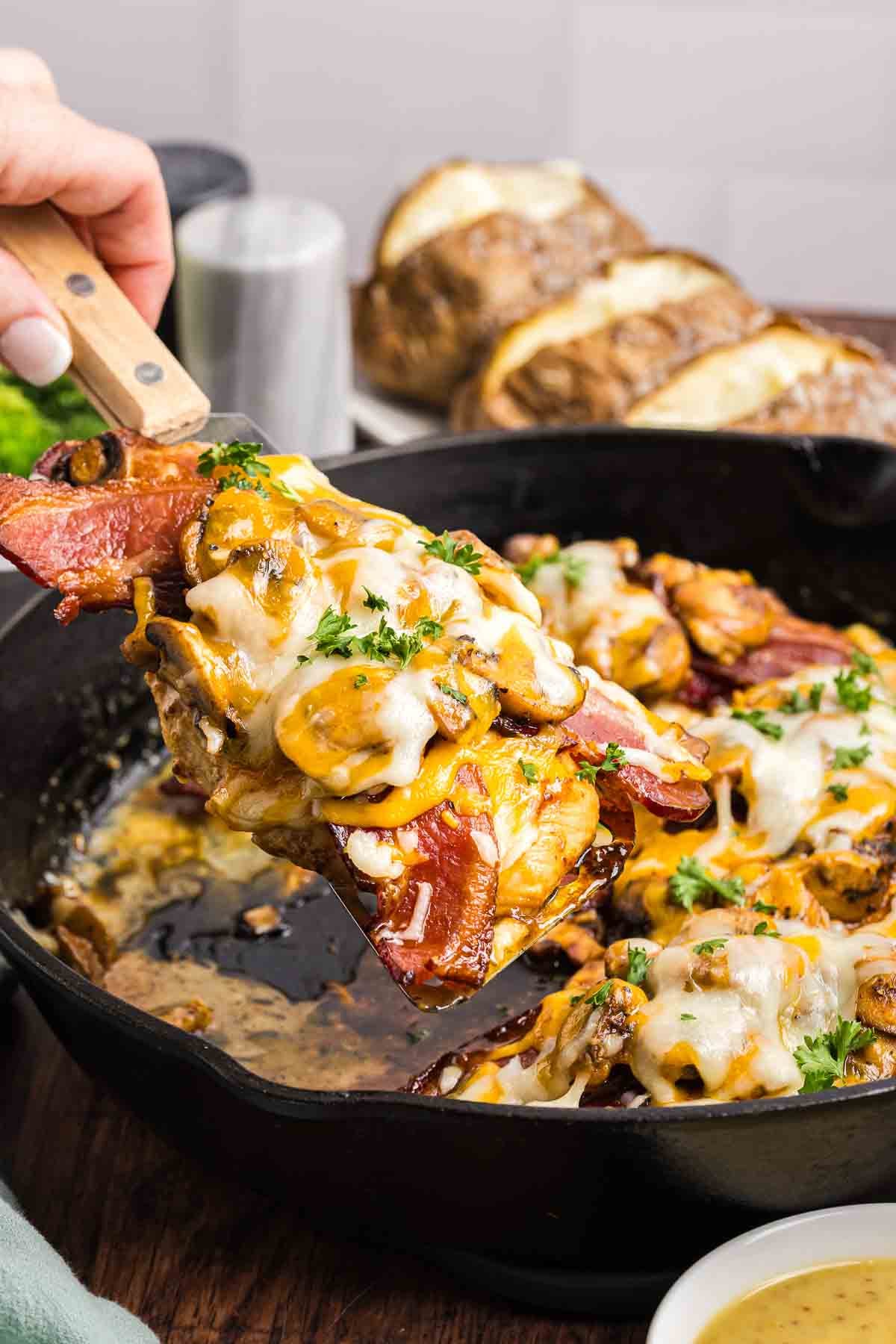 Scooping a piece of copycat alice springs chicken out of a cast iron skillet.