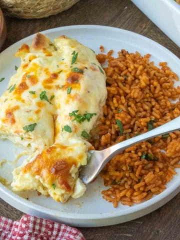 A plate of rotisserie chicken enchiladas with seasoned rice.