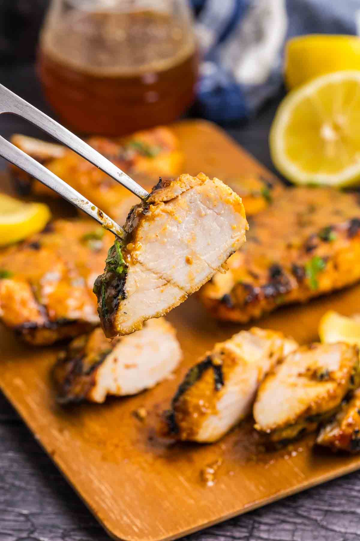 A serving fork picking up a piece of grilled chicken.
