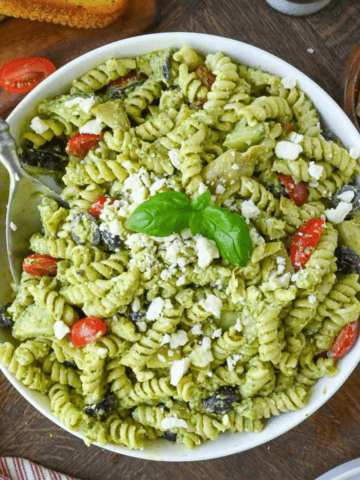 A close up of creamy pesto pasta in a white bowl.