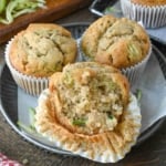 Three banana and zucchini muffins, one of which is half peeled and has a bite taken out of it.