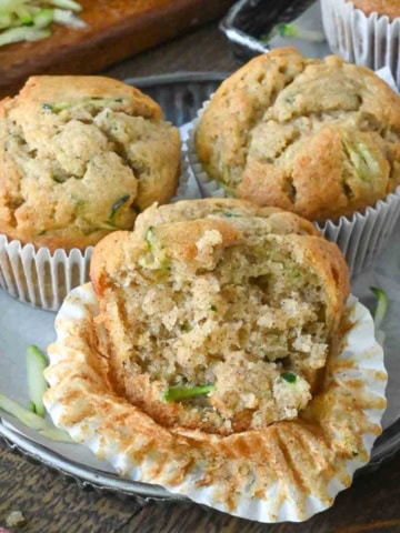 Three banana and zucchini muffins, one of which is half peeled and has a bite taken out of it.