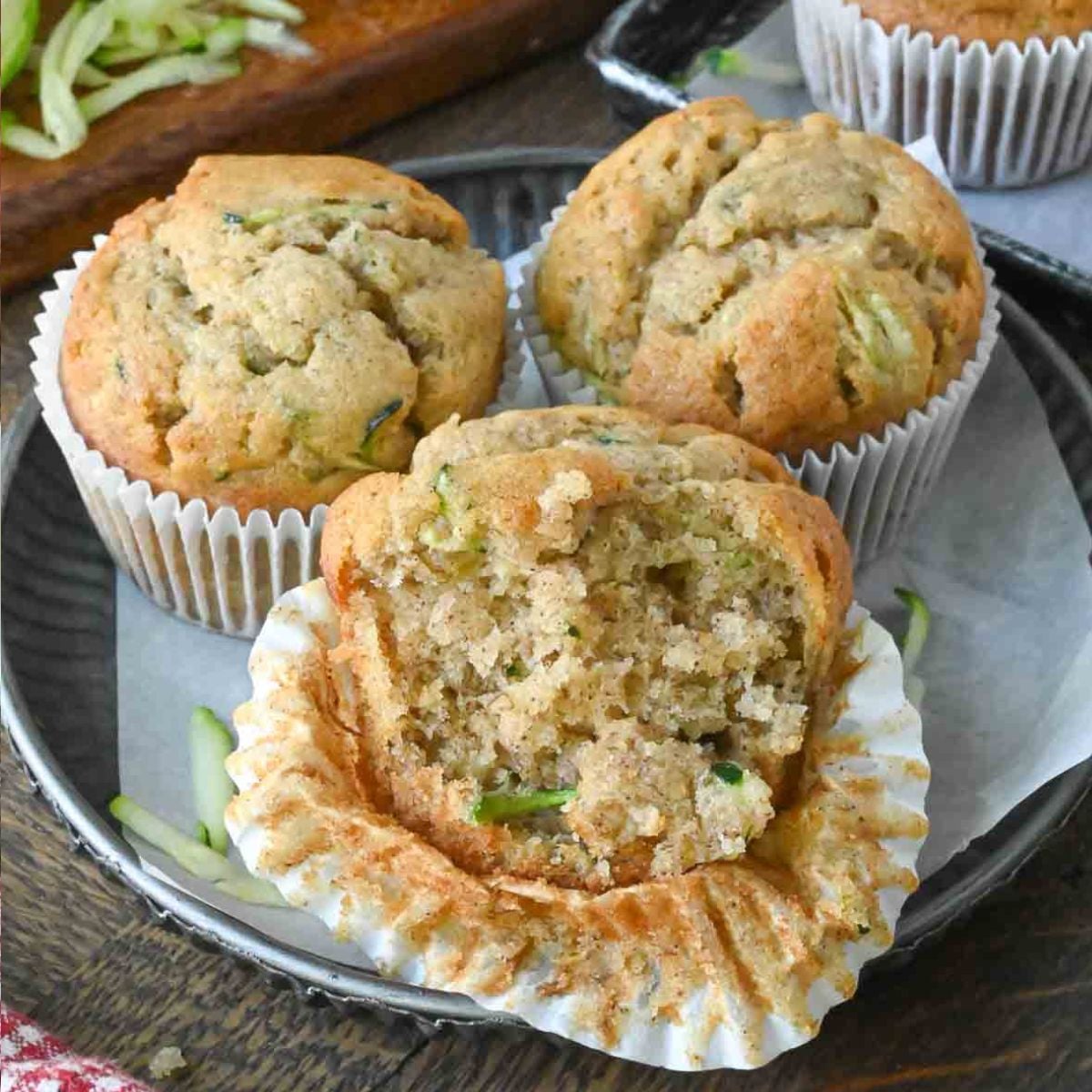Three banana and zucchini muffins, one of which is half peeled and has a bite taken out of it.