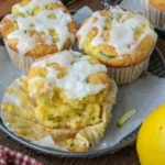 A plate of three lemon zucchini muffins, one of which has a bite taken out of it.