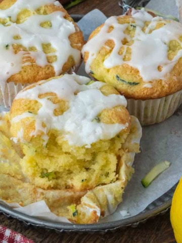 A plate of three lemon zucchini muffins, one of which has a bite taken out of it.