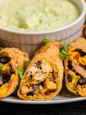 A plate of tex mex egg rolls with dipping sauce.