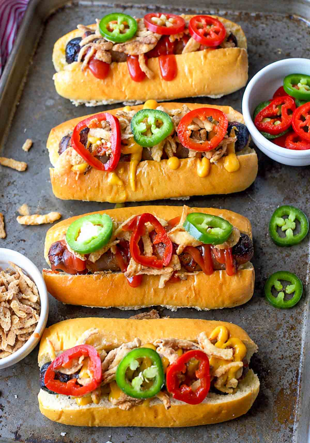 Four bacon wrapped hot dogs served on buns and topped with pepper slices.