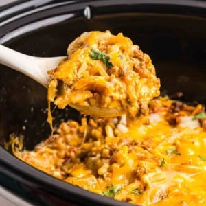 Taking a scoop of taco casserole from a slow cooker.
