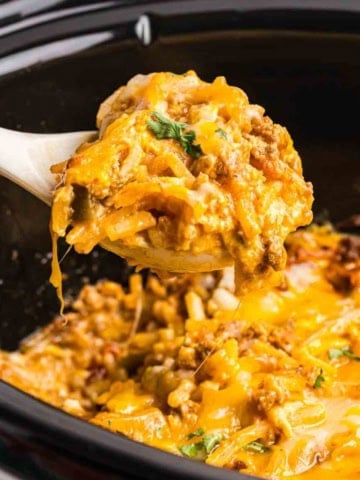 Taking a scoop of taco casserole from a slow cooker.