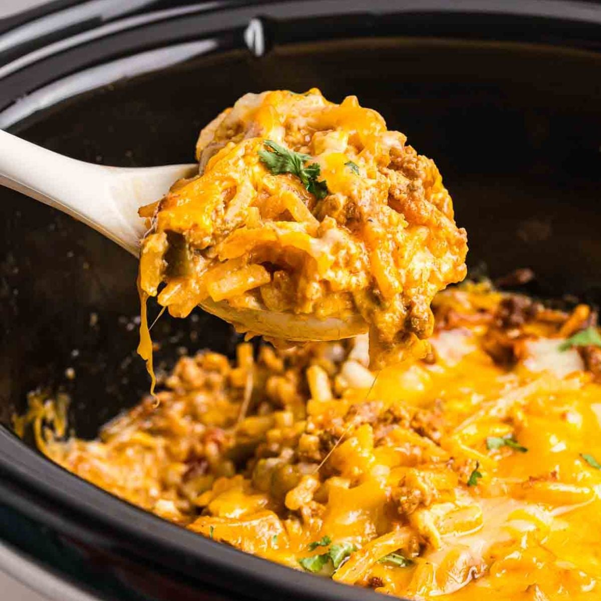 Taking a scoop of taco casserole from a slow cooker.