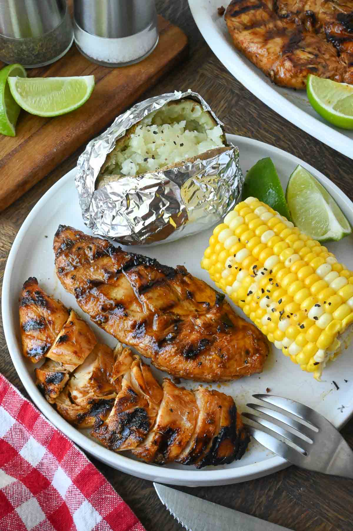A plate of chipotle honey chicken with corn on the cob and a baked potato.