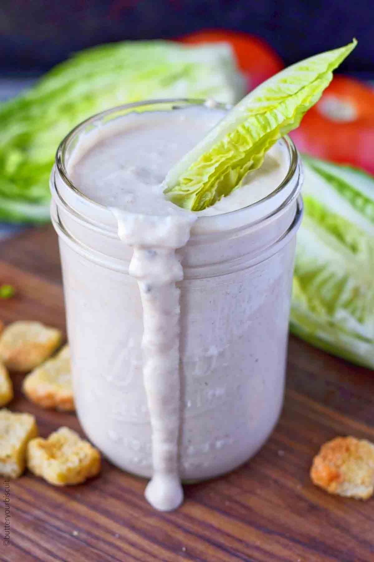 A jar of homemade caesar dressing with a single lettuce leaf.