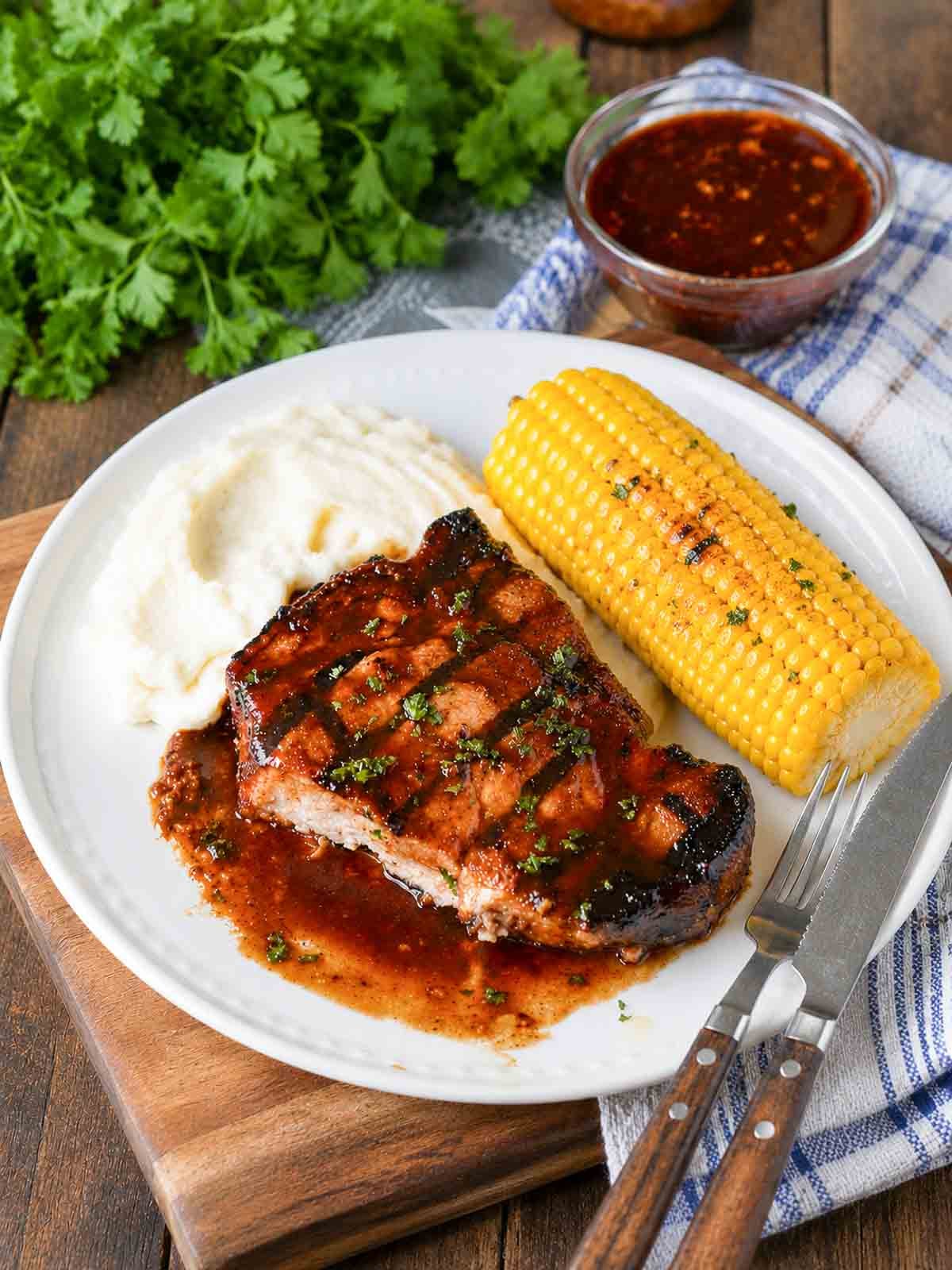Grilled hoisin pork chops on a plate with mashed potatoes and corn on cob.