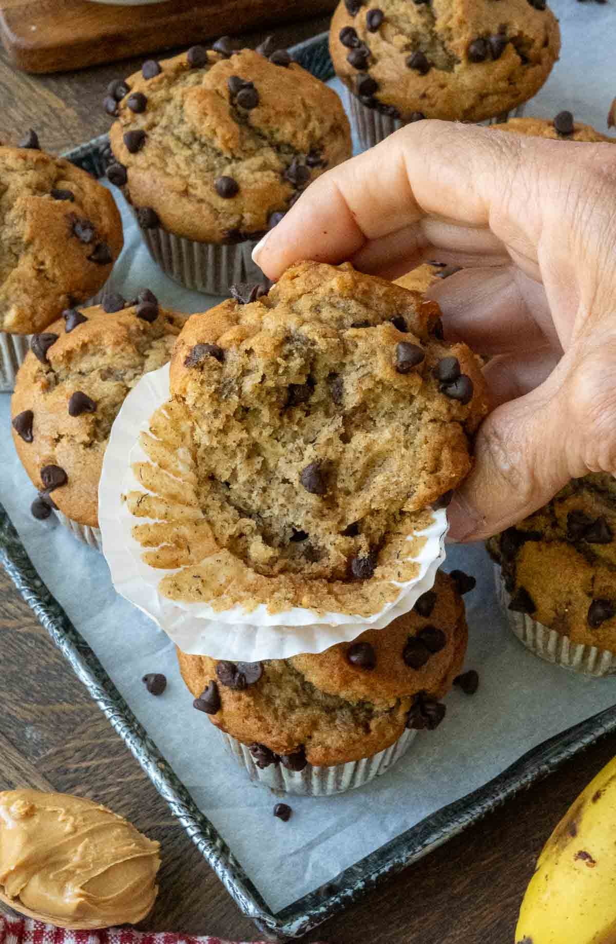 Holding up half of a peanut butter banana muffin with the liner partially peeled back.
