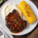 A close up of grilled hoisin pork chops served with mashed potatoes and corn on the cob.
